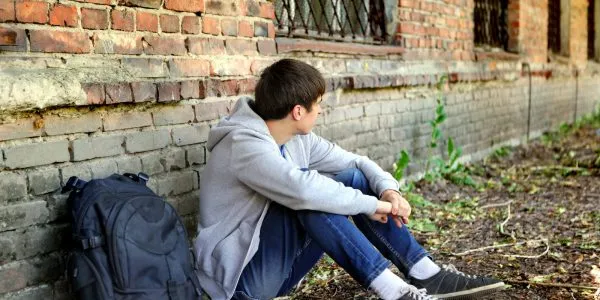 Одинокий и расстроенный подросток сидит возле кирпичной стены